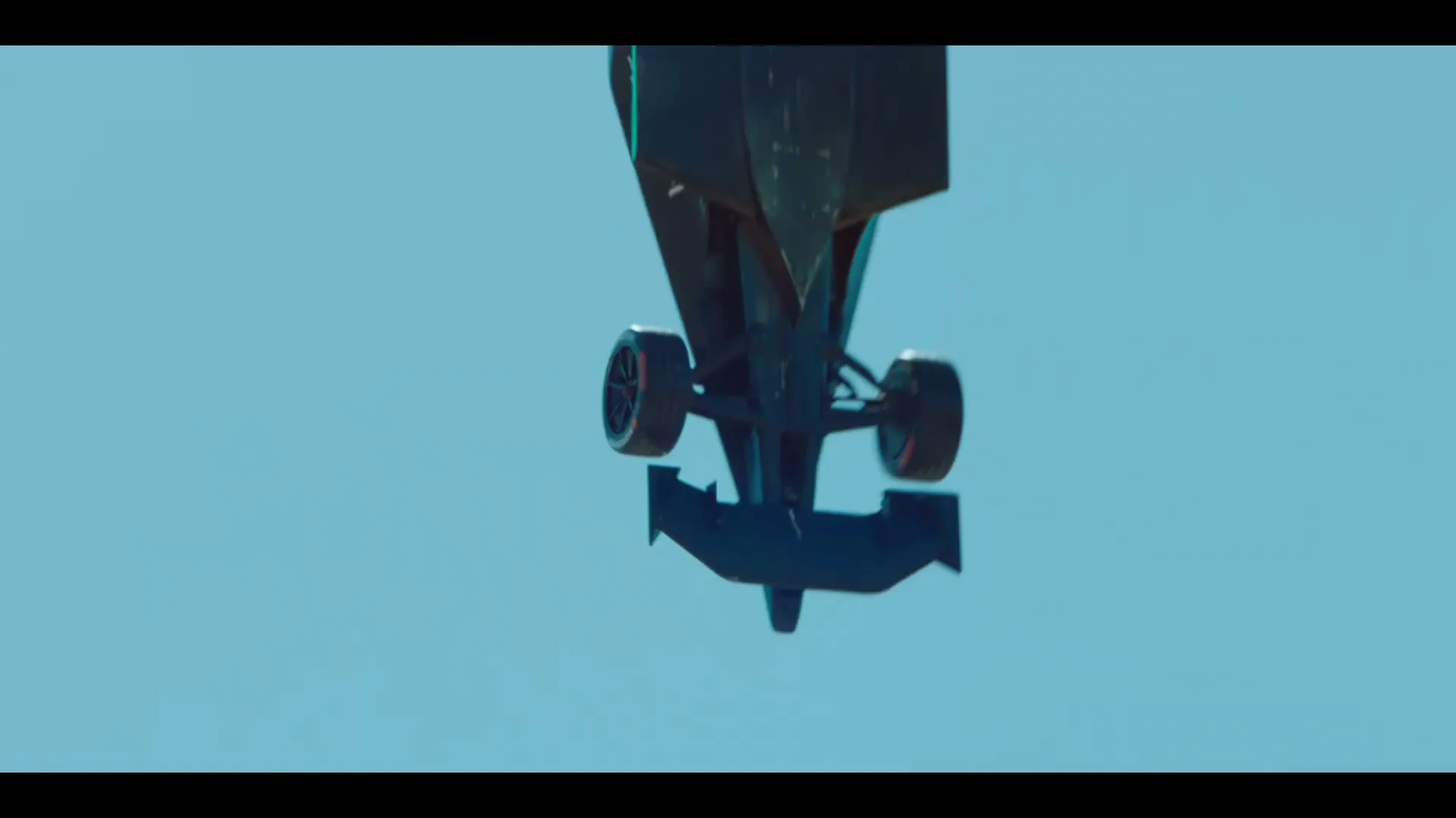 A Formula E race car, black with vibrant pink and green accents, is seen from an overhead perspective, driving on a bright blue background.
