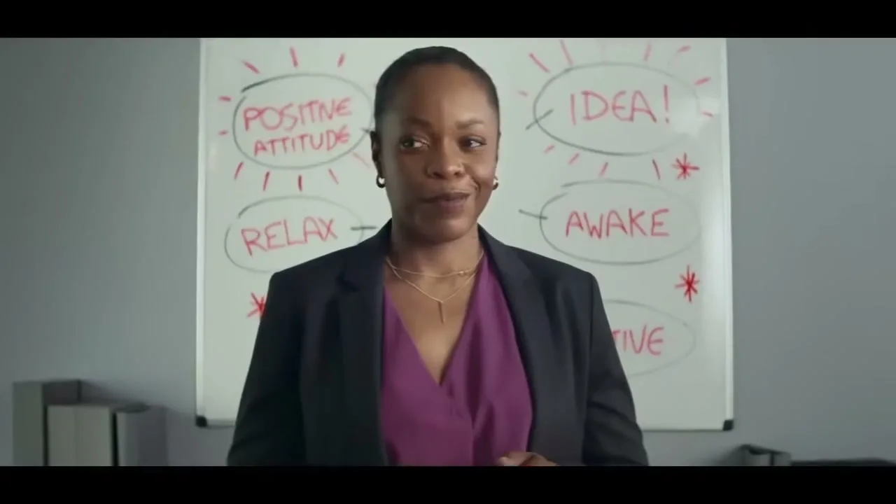 A Black woman in a business suit stands in front of a whiteboard with "POSITIVE ATTITUDE," "RELAX," "IDEA!," and "AWAKE" written on it.
