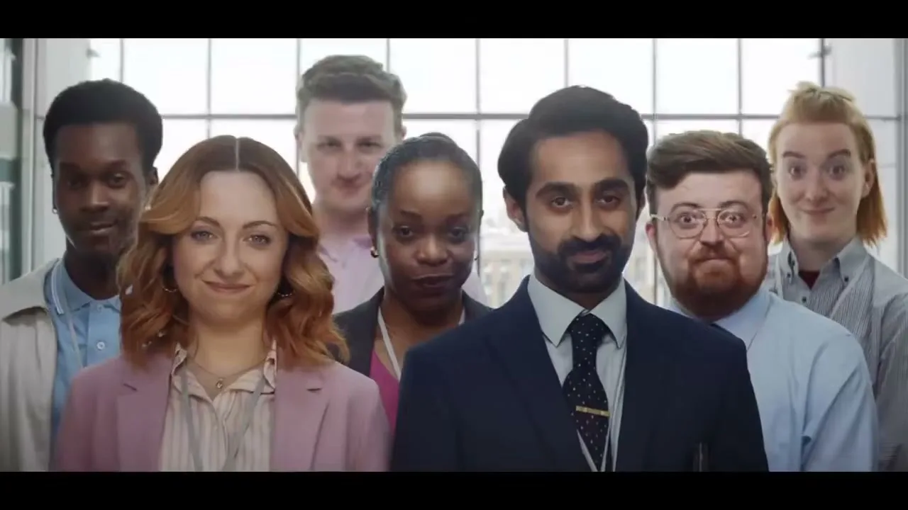 A diverse group of seven office workers, dressed in business casual attire, stand together in an office, raising their eyebrows playfully.