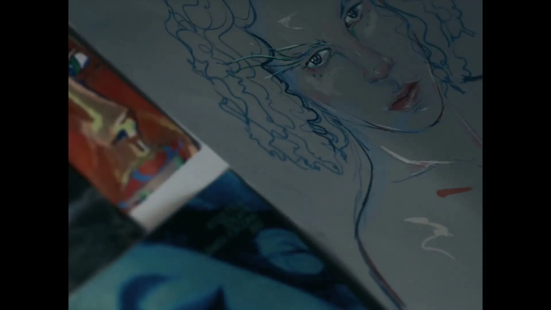A close-up shot of a drawing of a person's face with curly hair and blue eyes, surrounded by other drawings, in an interior setting.
