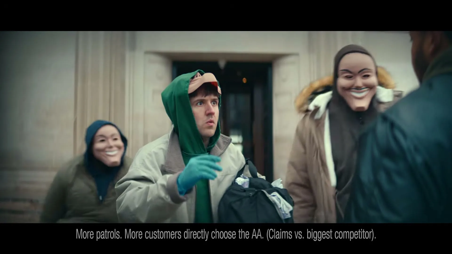 Three masked people in hoodies and jackets approach a man, then remove their masks to reveal surprised expressions, outside a building.