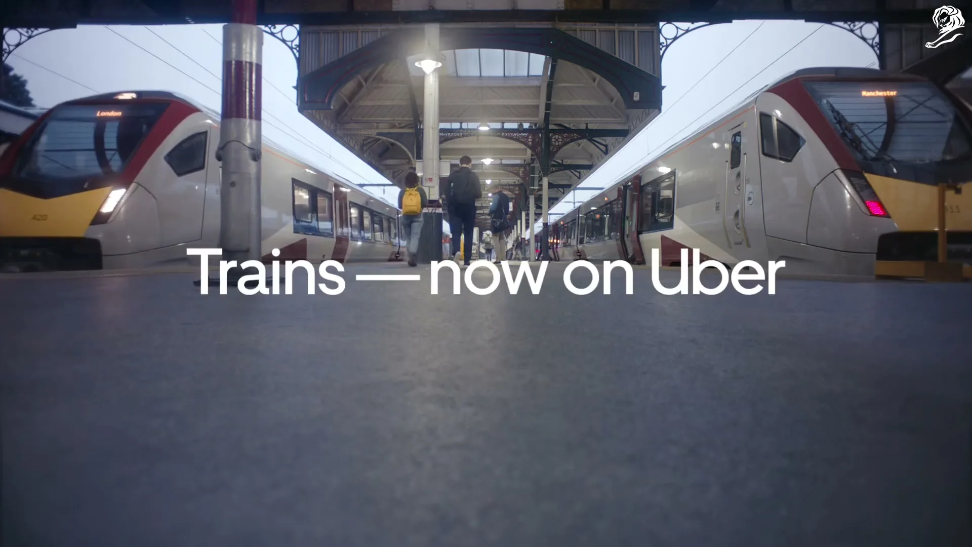A low-angle shot of a train station platform with two trains on either side, and people walking towards the camera.