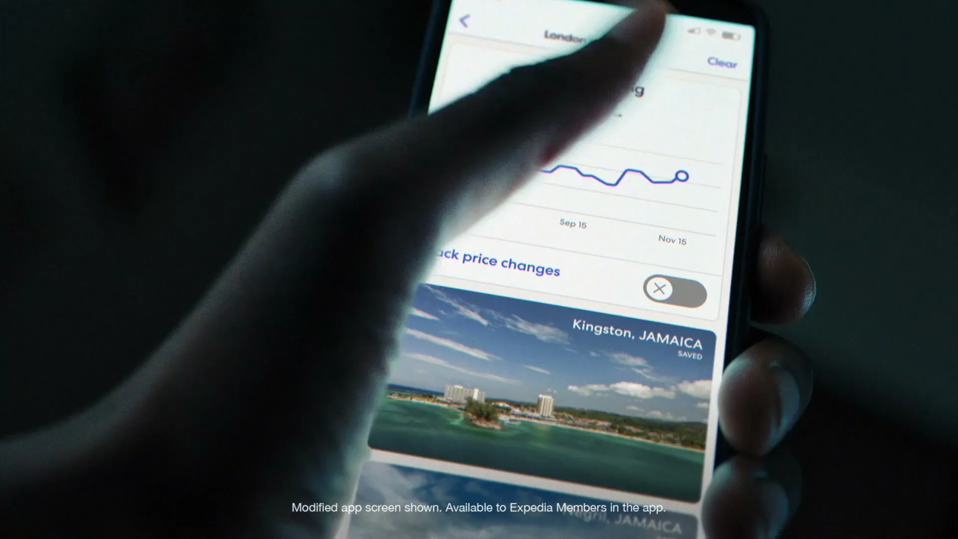 A person's hand holds a smartphone, tapping to activate price tracking for a flight to Kingston, Jamaica, on the Expedia app.