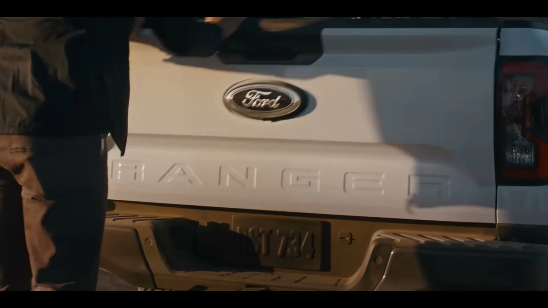 A person in dark clothing closes the tailgate of a white Ford Ranger pickup truck, revealing the Ford logo and Ranger text.