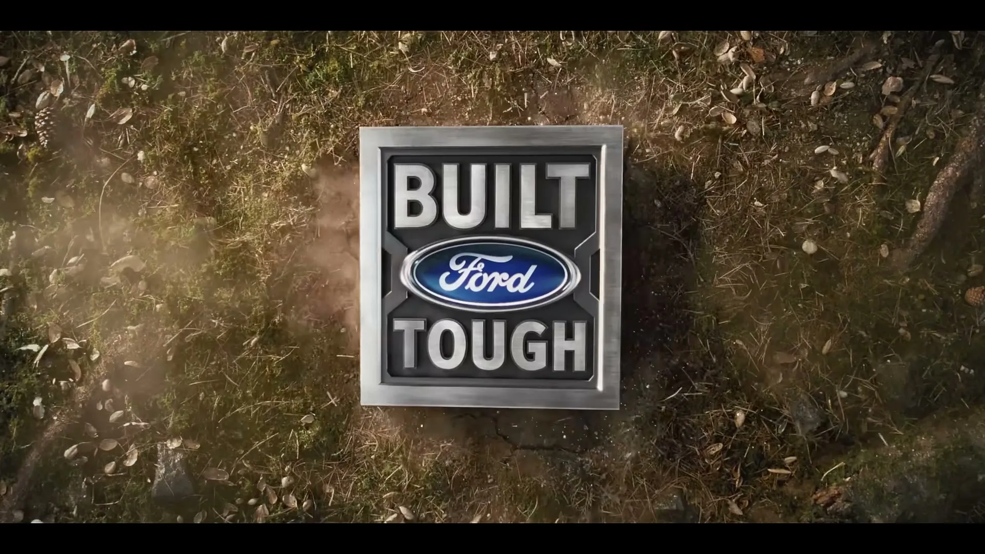 The Ford "Built Tough" logo is centered on screen, surrounded by dirt and leaves, as dust puffs up around it.
