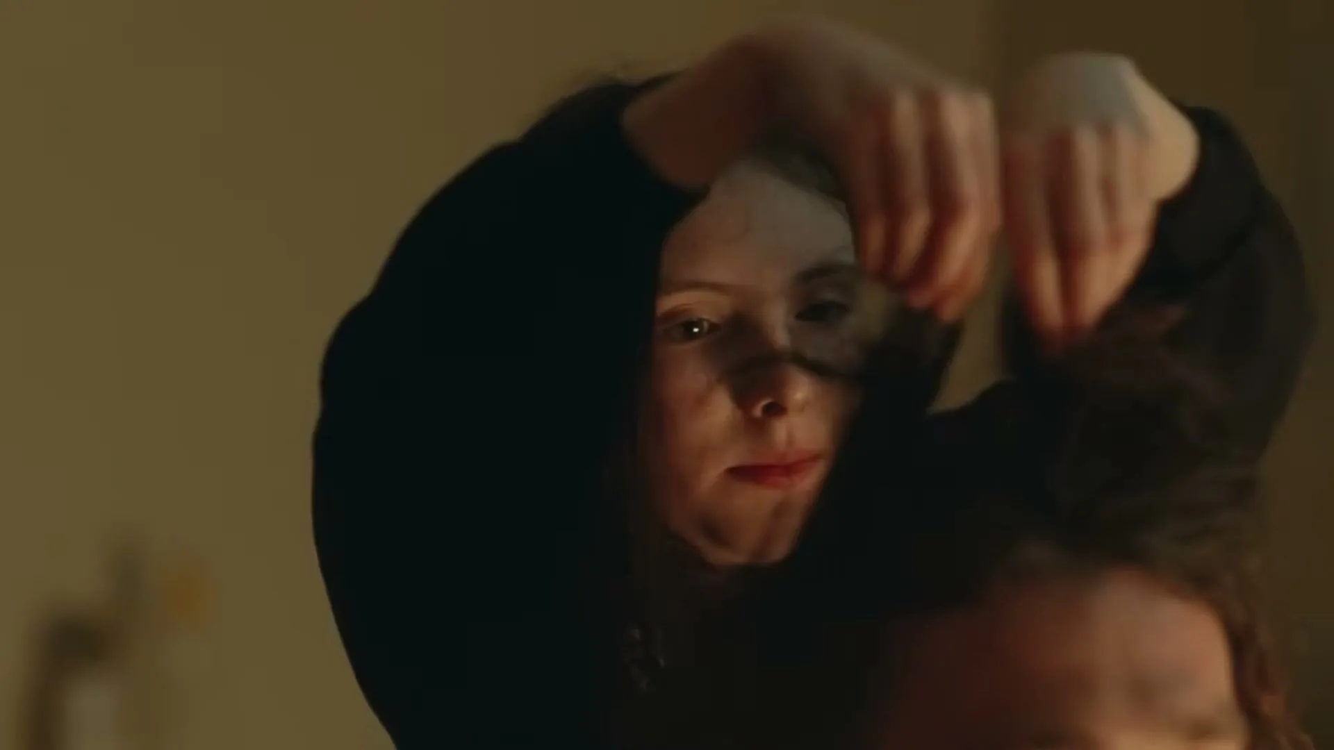 A young girl with dark hair and freckles gently plays with the hair of another person, her expression soft and focused.