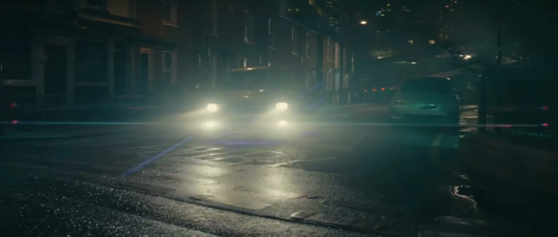 A bright yellow car with glowing headlights and underglow speeds down a wet, dark city street at night, passing parked cars and buildings.