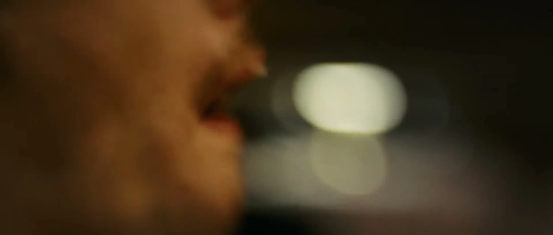 A blurry extreme closeup of a person's mouth, slightly open, with bokeh lights in the background, in an interior setting at night.