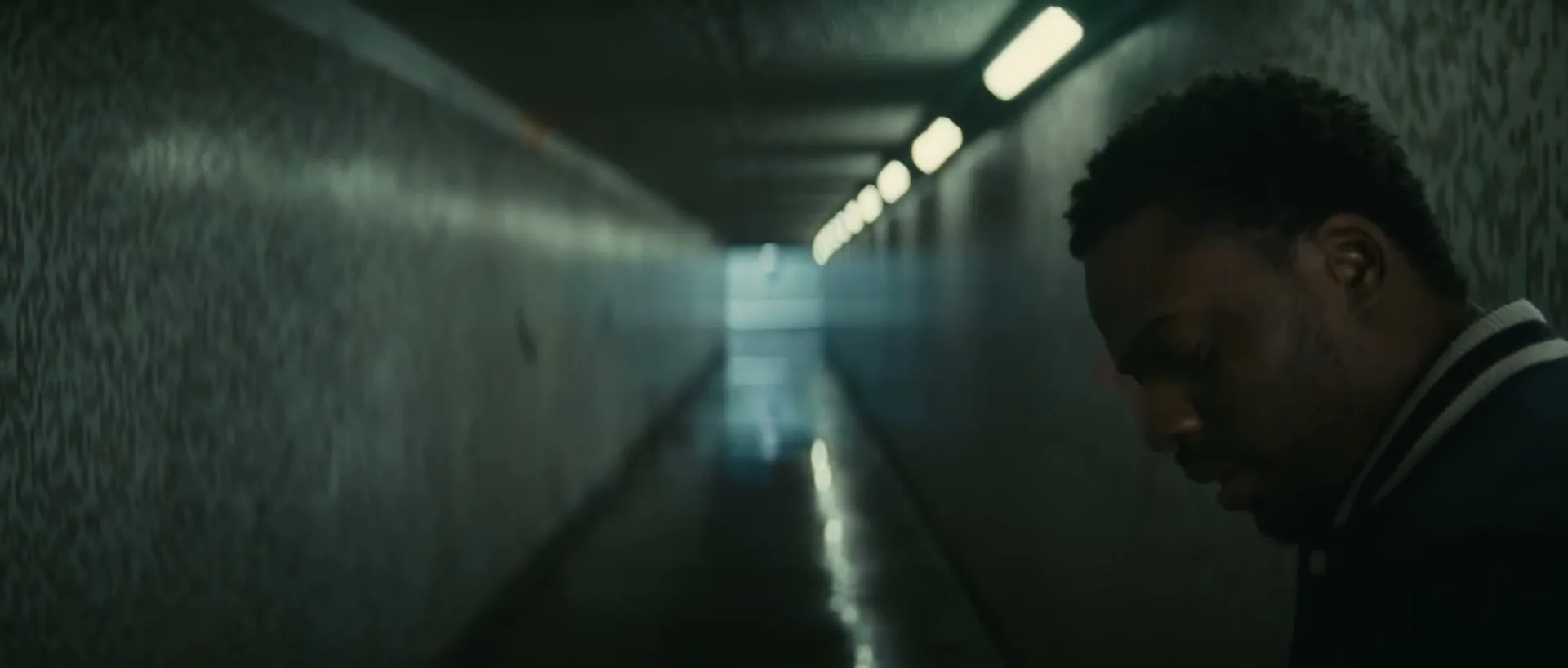 Two men, one with blonde hair and one with dark hair, walk through a dimly lit, graffiti-covered underpass, looking around cautiously.