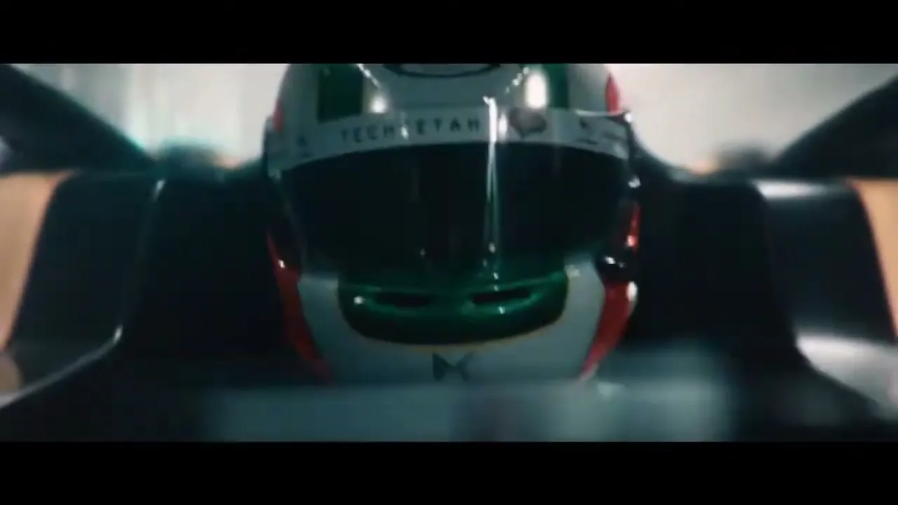 A close-up shot of a race car driver's helmet, with green, white, and red stripes, as the car speeds forward in a tunnel.