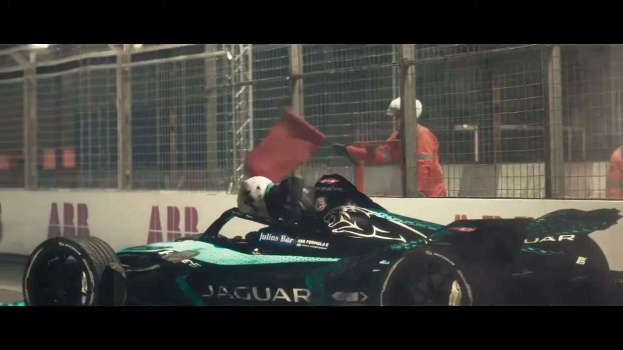 A Formula E race car, black and teal, speeds past a track worker waving a red flag at night on a race track.
