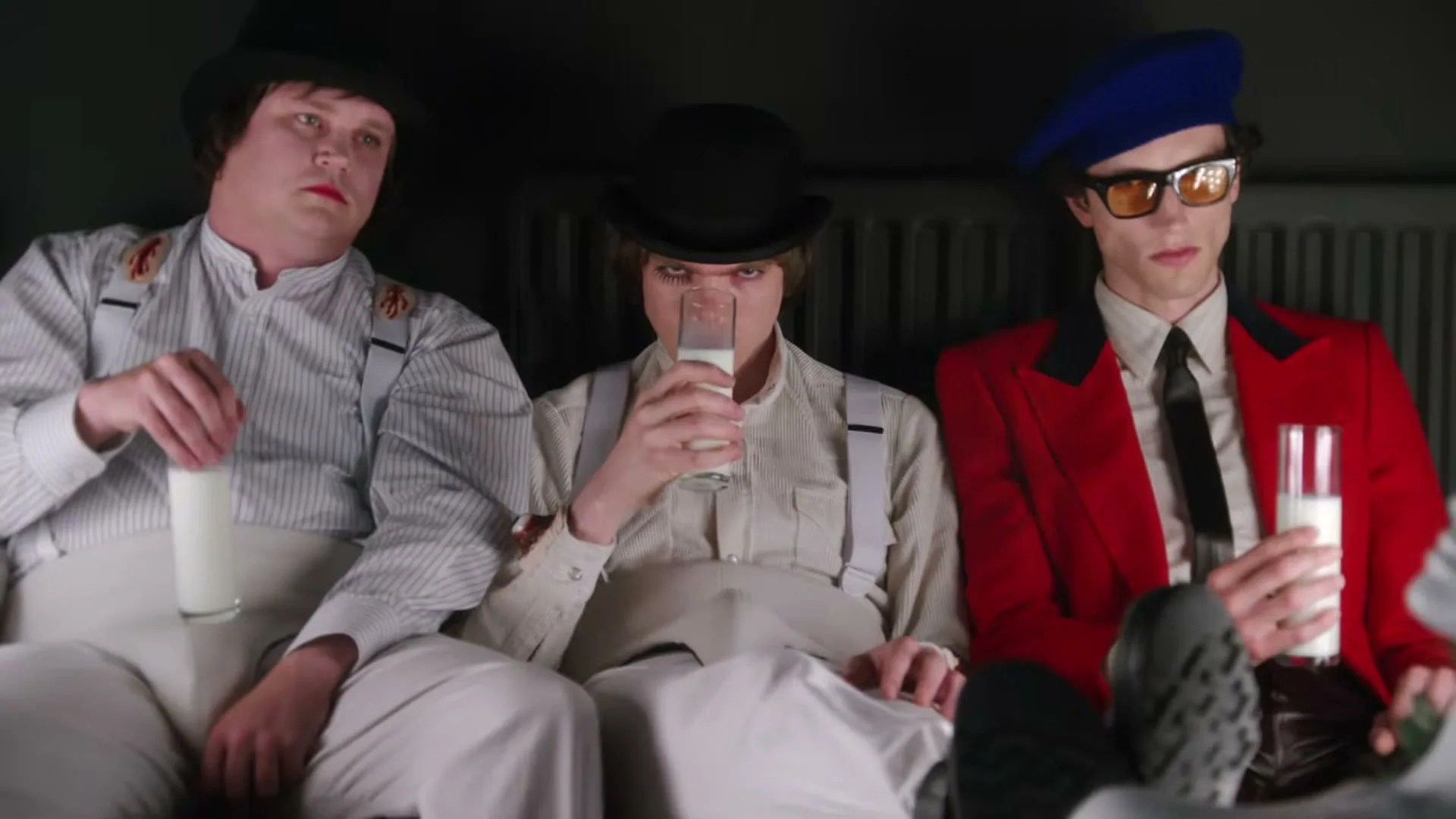 Three men in bowler hats and suspenders, dressed in a Clockwork Orange style, sit together drinking milk.