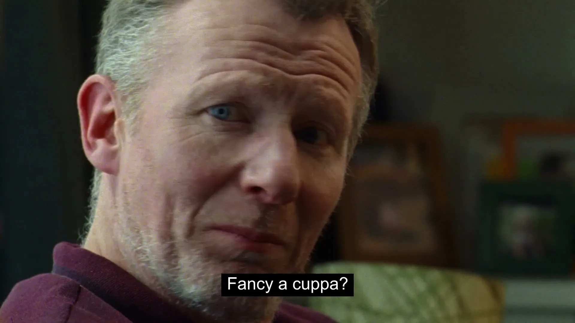 A middle-aged man with grey hair and a beard looks up and smiles, asking "Fancy a cuppa?" in a warm, inviting tone.