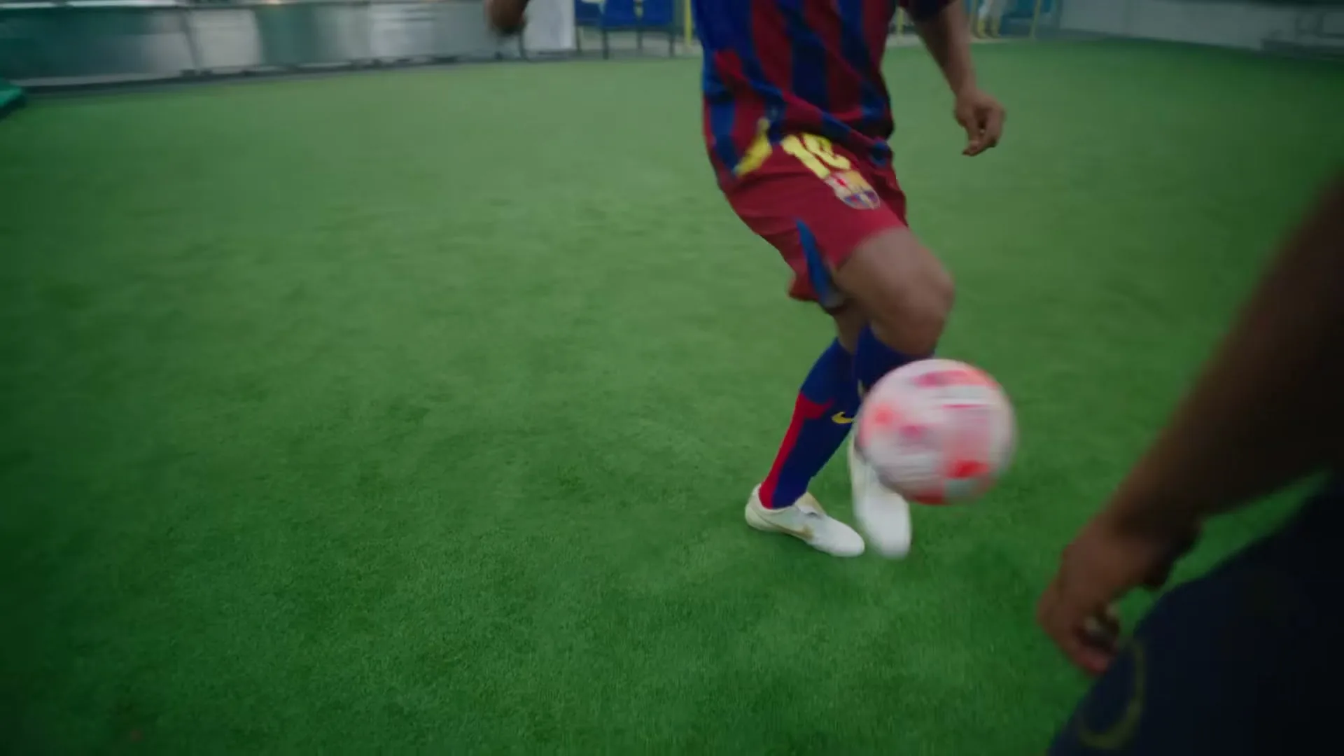 A male soccer player in a red and blue striped jersey with the number 10 on it, dribbles a soccer ball on a green indoor field.