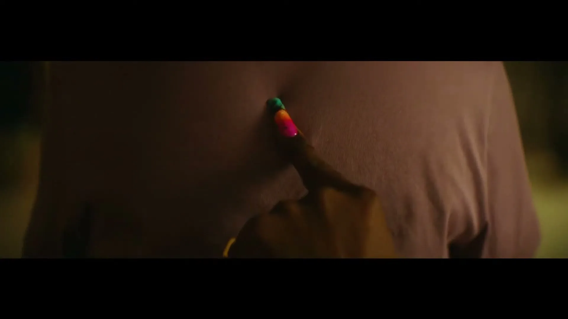 A person with a colorful painted fingernail gently pokes another person's back, who is wearing a light purple t-shirt, in a dimly lit interior.