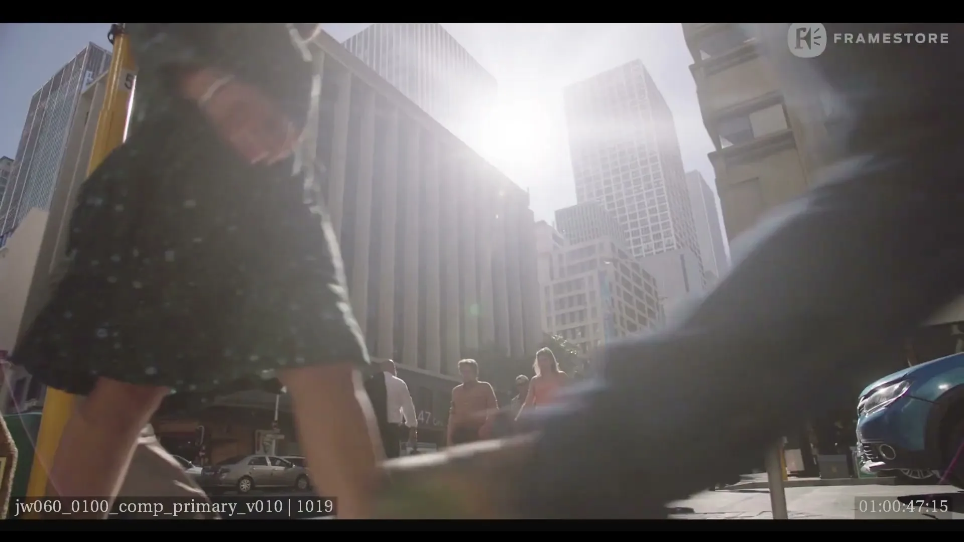 A low-angle shot of a busy city street with pedestrians walking past, and tall buildings in the background under a bright sky.