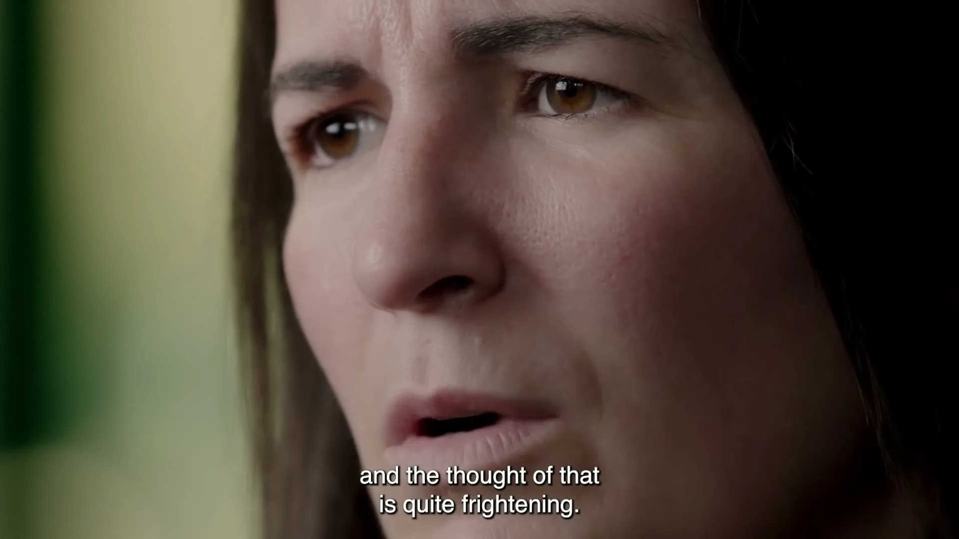 A woman with dark hair and a concerned expression speaks, looking slightly off-camera in an interior setting.