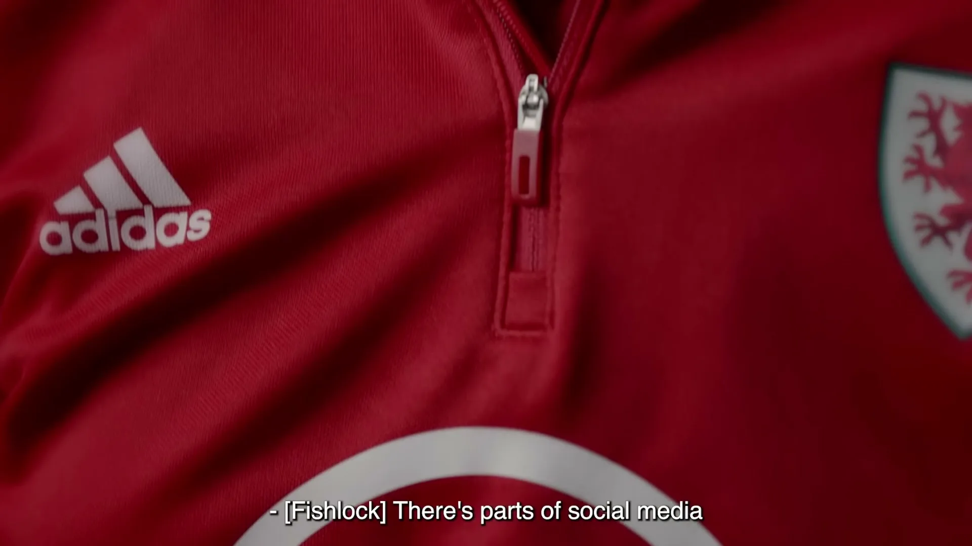 A close-up shot of a person wearing a red Adidas sports jacket with a white BT logo and a Welsh dragon emblem.