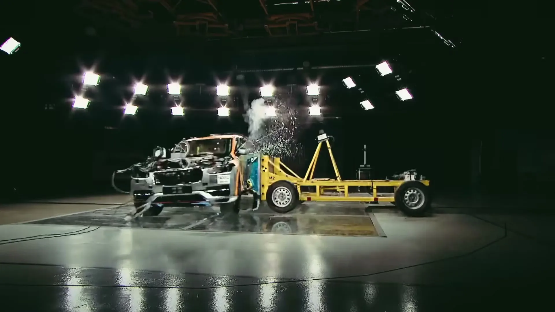 A Volvo car undergoes a side-impact crash test in a dimly lit, high-tech testing facility, with debris flying upon impact.