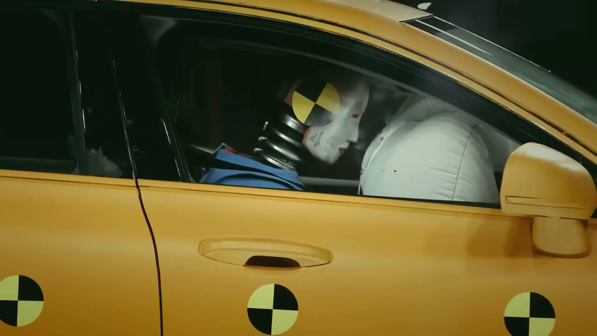 A crash test dummy in a yellow car is seen from the side, as an airbag deploys and then retracts after impact.
