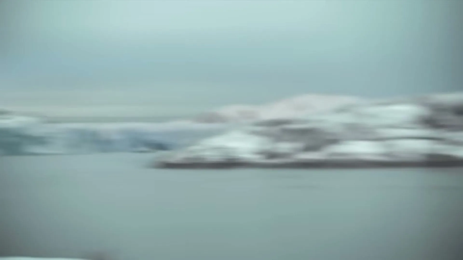 A man in a winter coat and hat stands in front of a snowy landscape, then a glacier calves into the water.