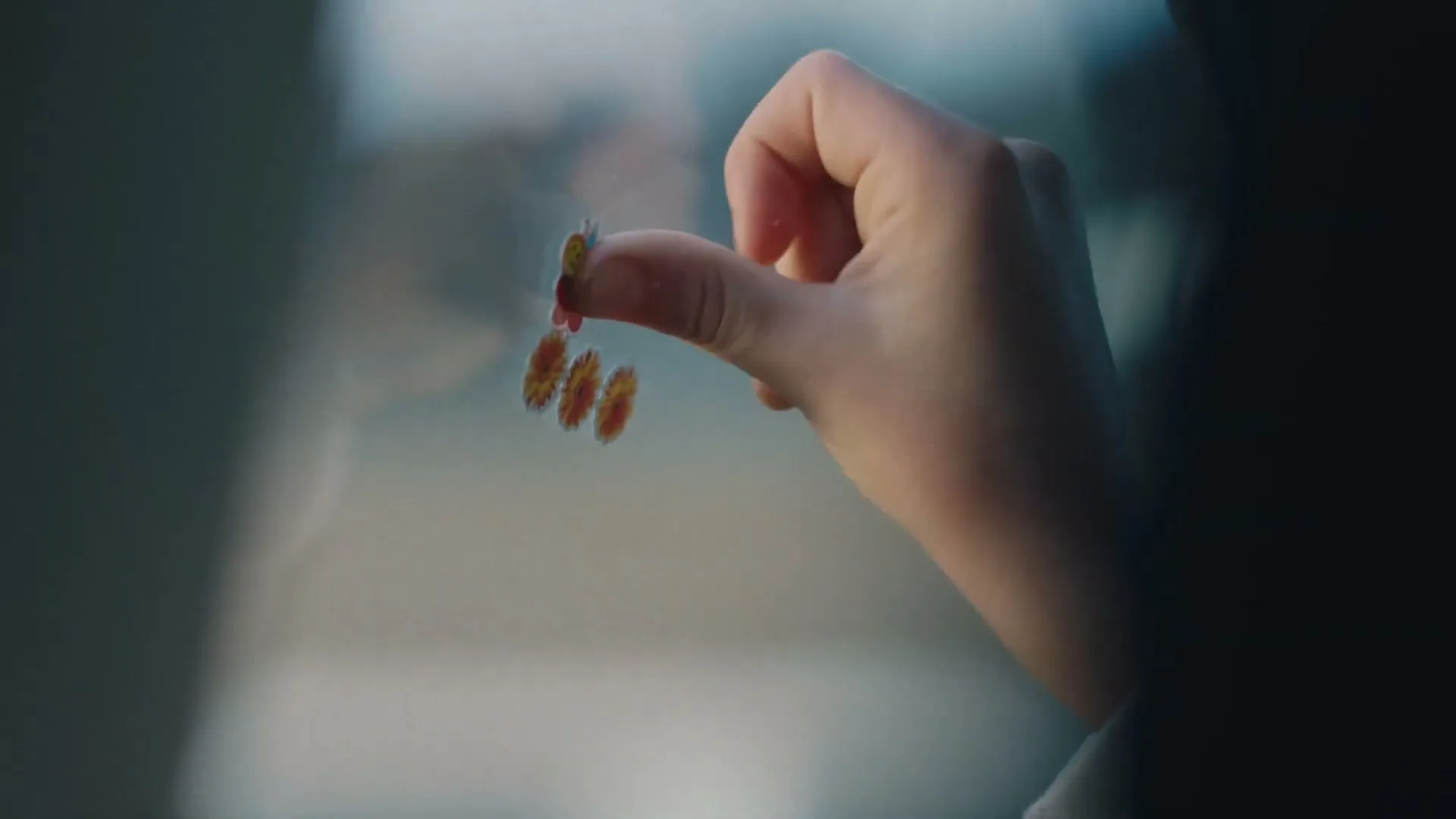 A child's hand places a small bee sticker on a window, with other flower stickers already present, in a soft focus interior.