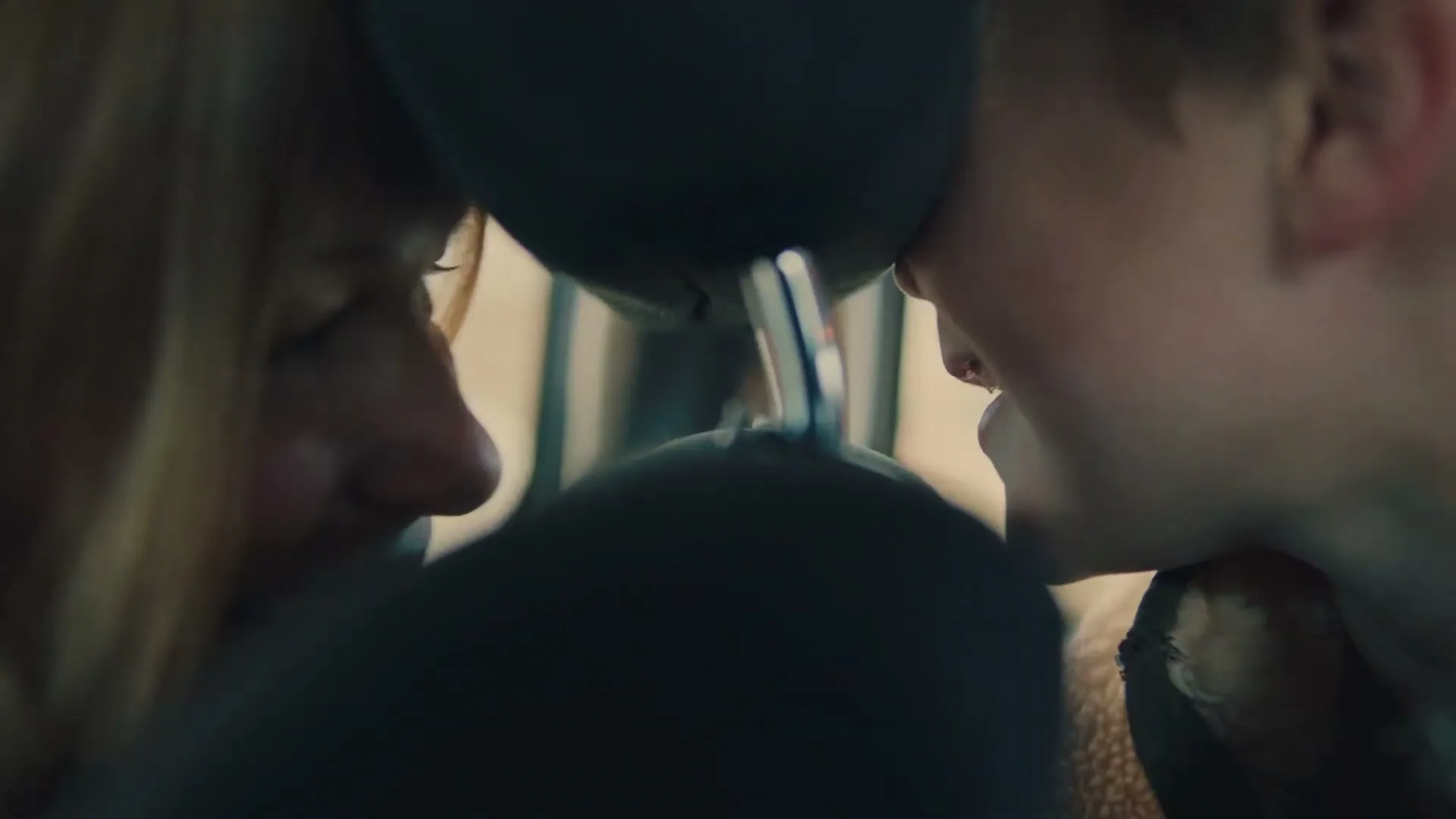 A young boy and a woman are seen in a car, with the boy's face close to the back of the car seat, and the woman smiling at him.