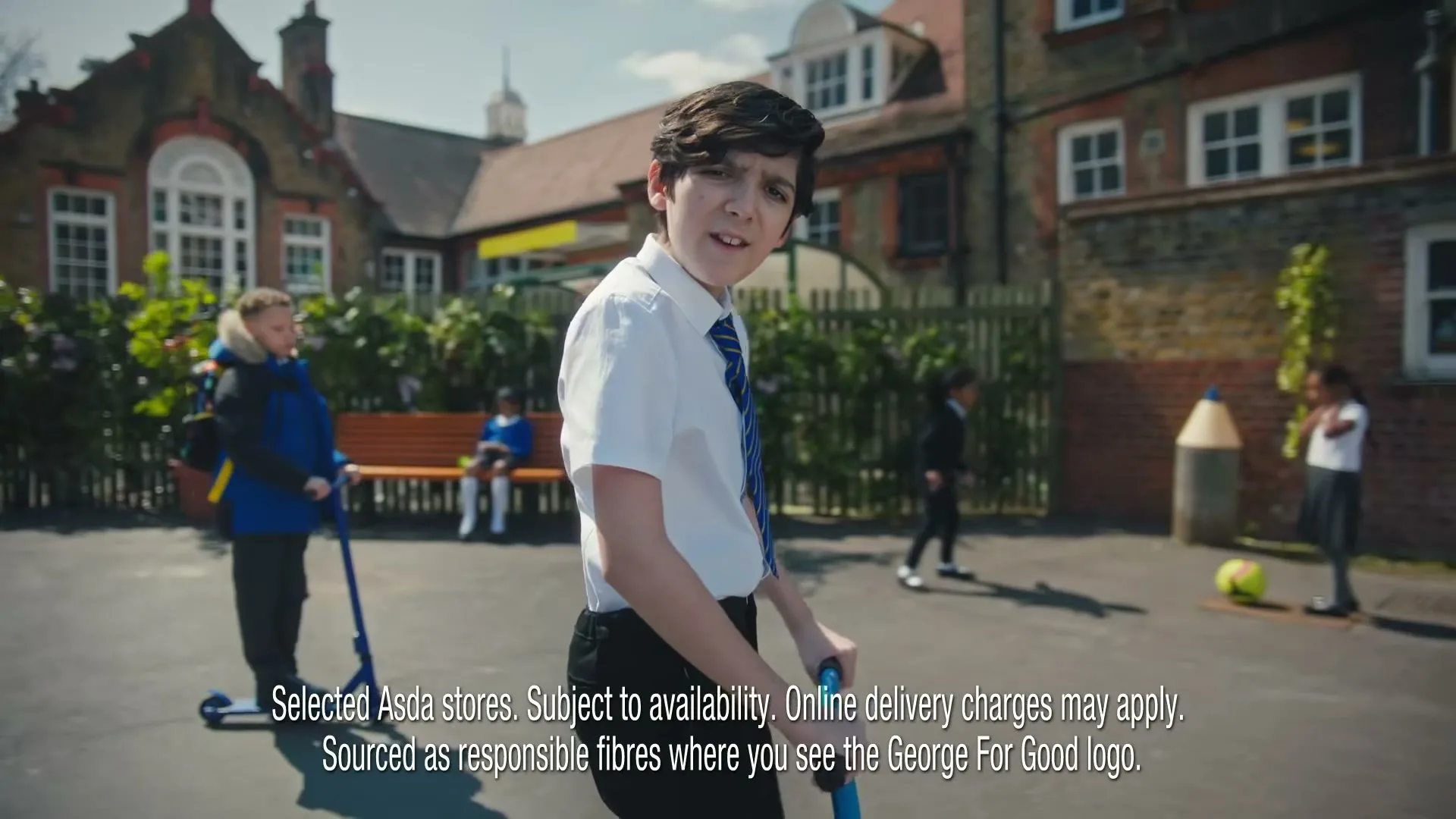 A young male student in a white shirt and blue tie rides a scooter in a schoolyard, looking back at the camera.