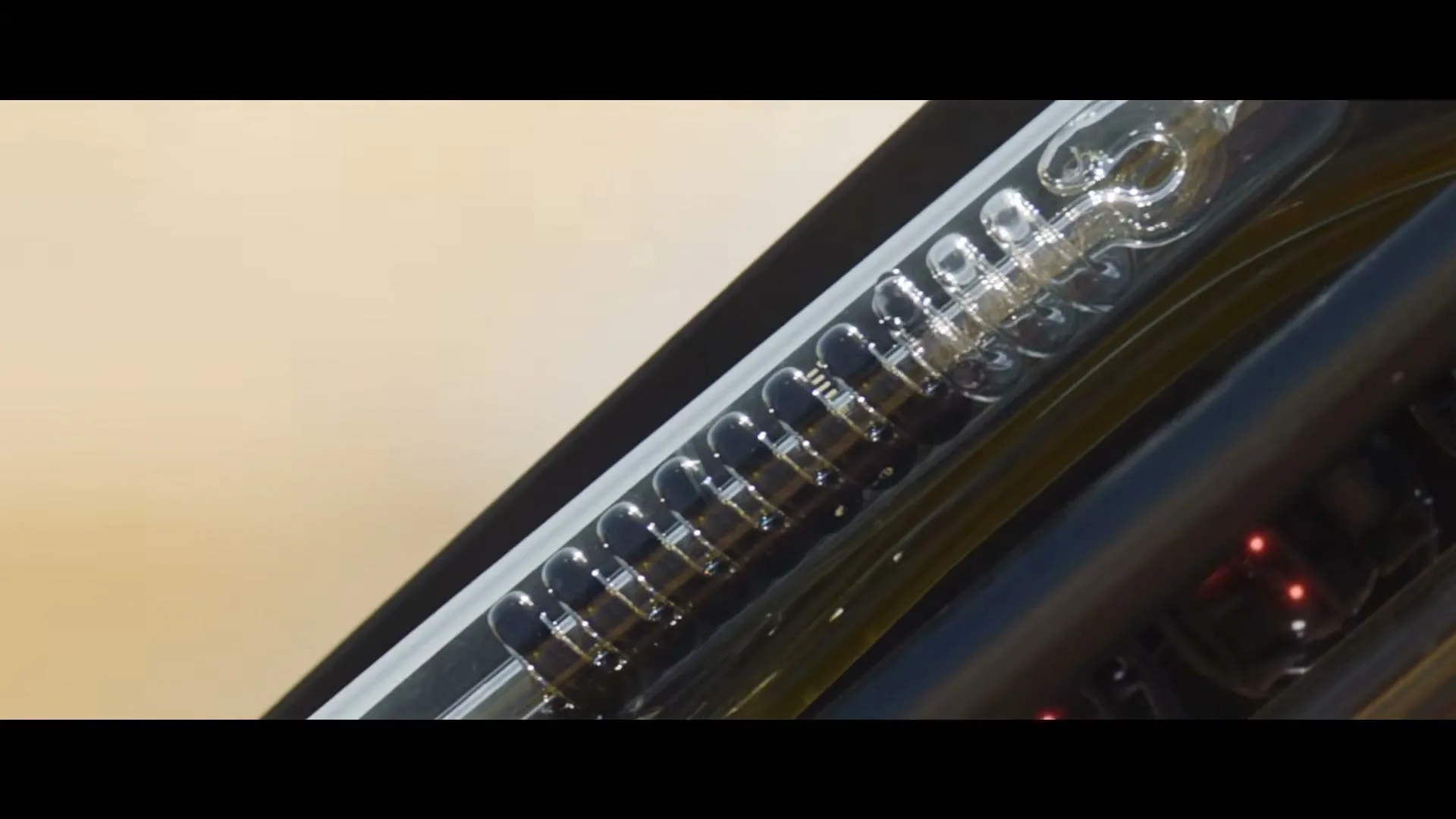 A close-up shot shows a clear glass tube with a spring inside, part of a robot's inner workings, with small red and green lights visible.