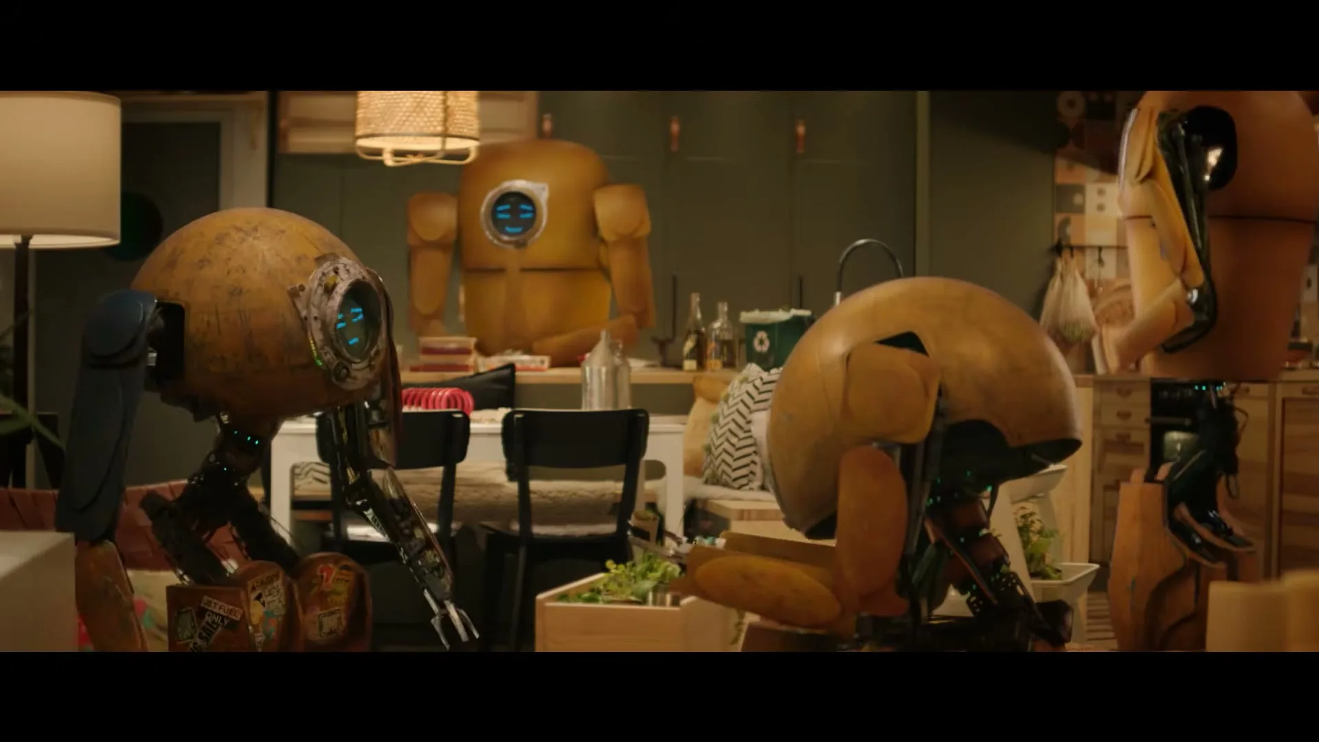 Three small, yellow, round robots with blue accents are seen in a medium shot, looking at a larger robot in a cozy living room.