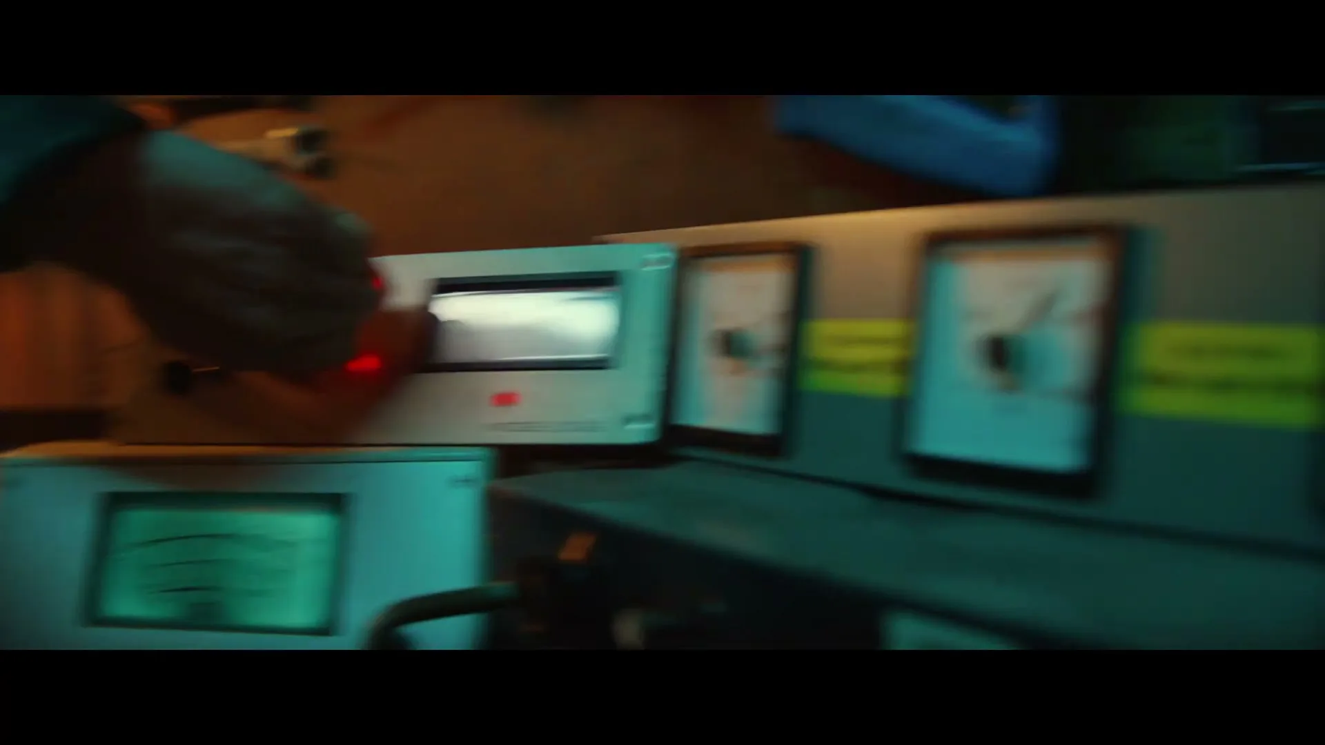 A person's hand adjusts a dial on a vintage-looking control panel with multiple gauges and lights, in a dimly lit, industrial setting.