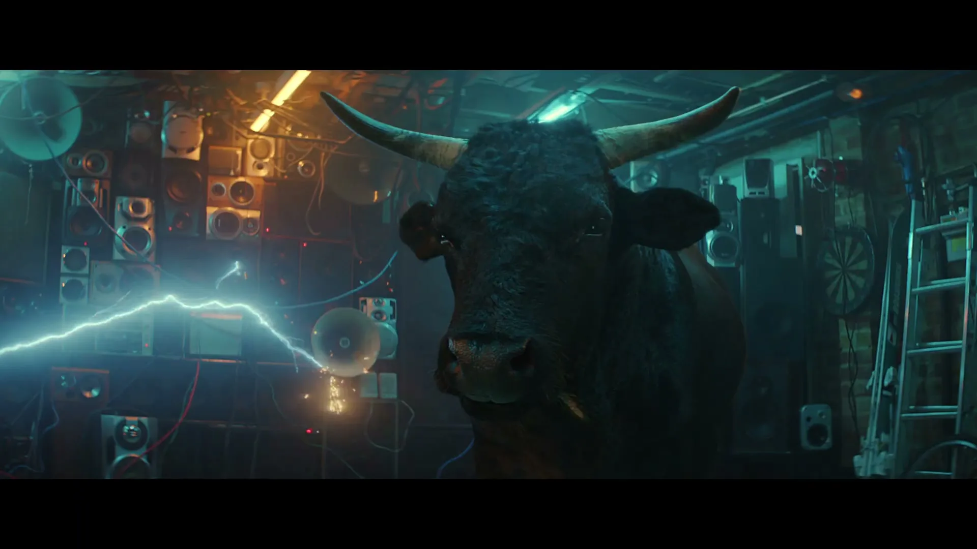 A large, dark bull stands calmly in a cluttered room filled with speakers and electronic equipment, as electricity sparks around it.
