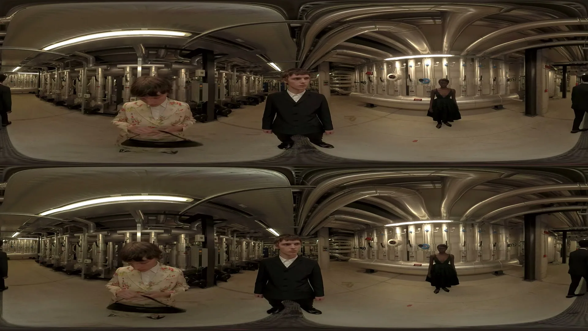 Four models, two male and two female, are seen in a split-screen view, posing and looking at the camera in a futuristic, industrial-style room with pipes and machinery.