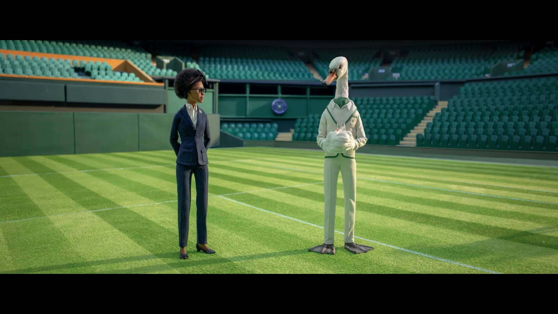 A woman in a suit and a swan-headed man in a tennis outfit stand on a tennis court in a stadium, talking.