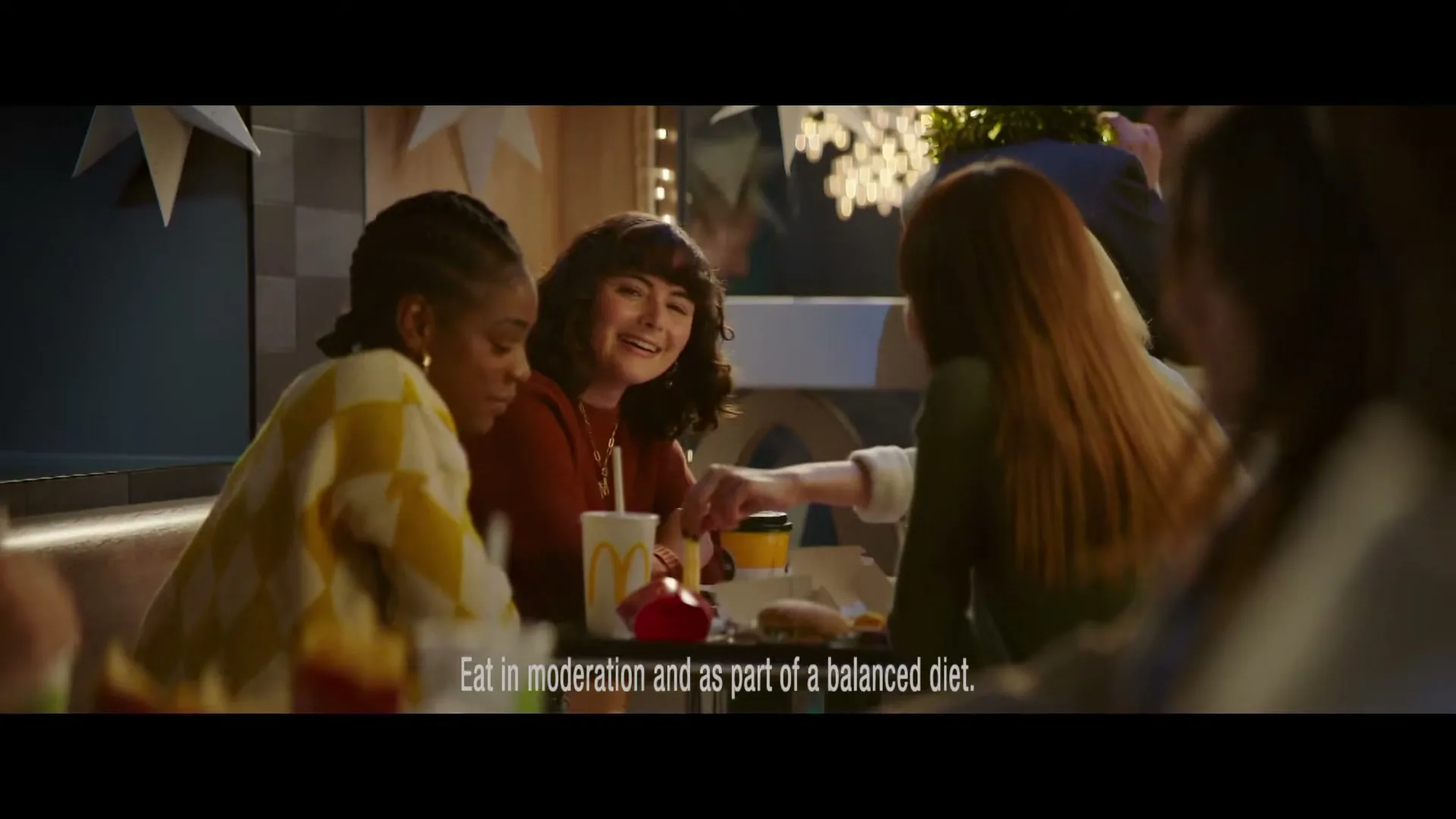 Three young women are sitting at a booth in a McDonald's restaurant, laughing and eating fast food.