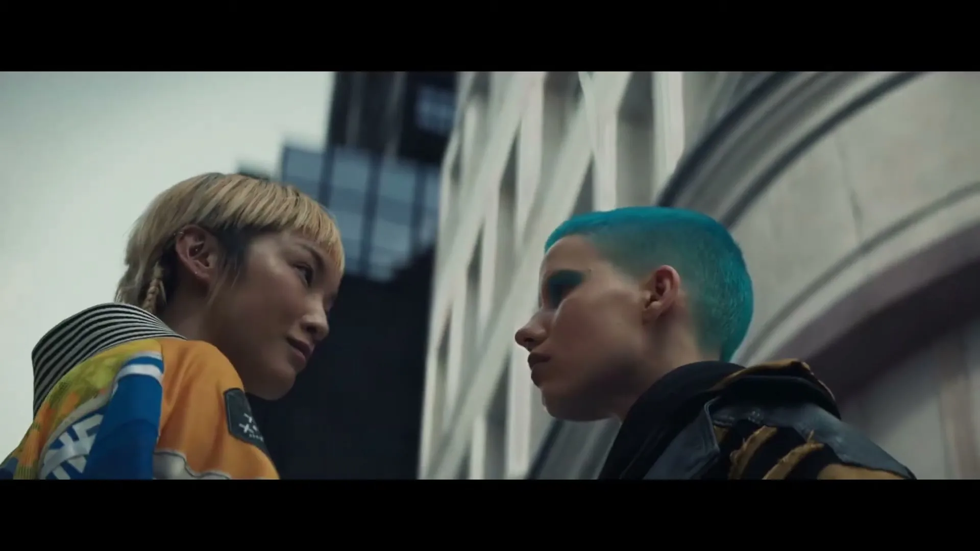 Two young women, one with blonde hair and the other with blue hair, face each other intensely on a city street.