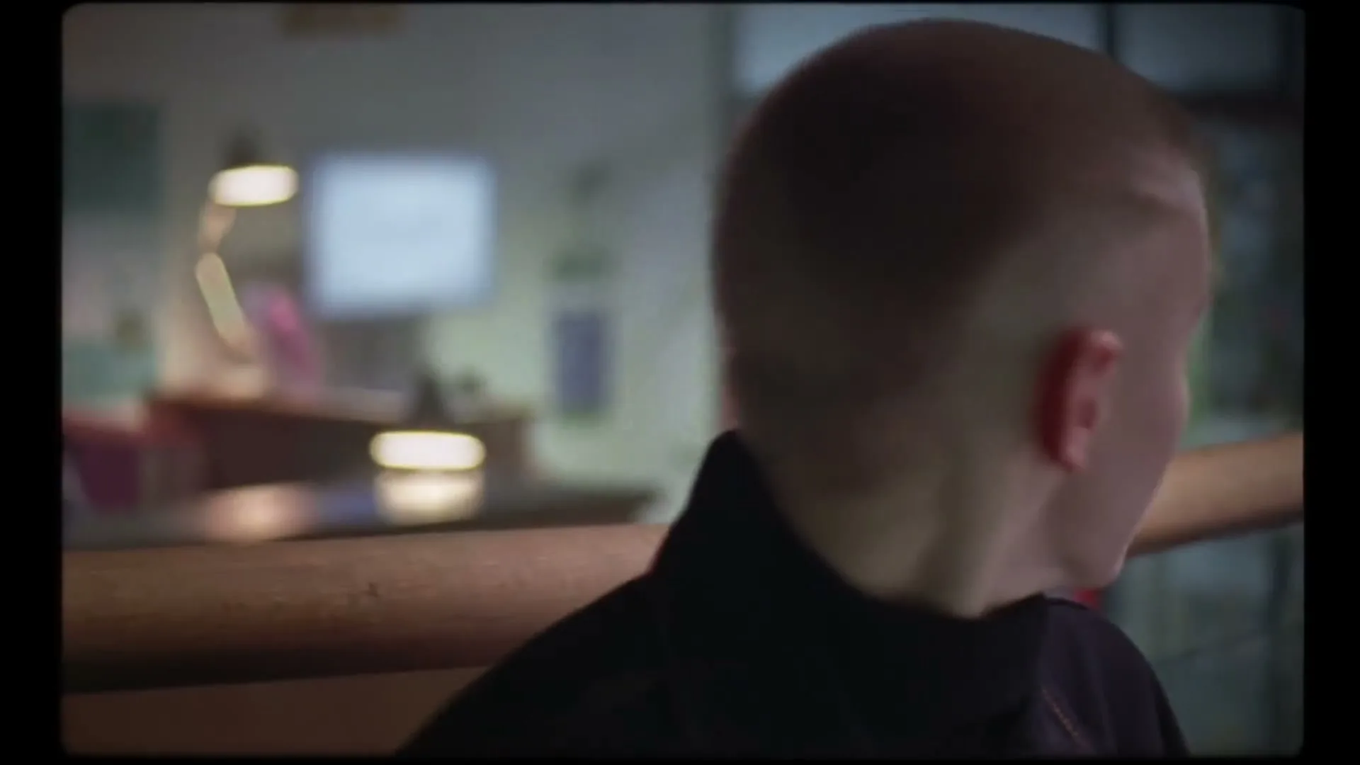 A young person with a buzzcut looks around a waiting room, then turns to look at a screen displaying "Jemma Miller Room 4."