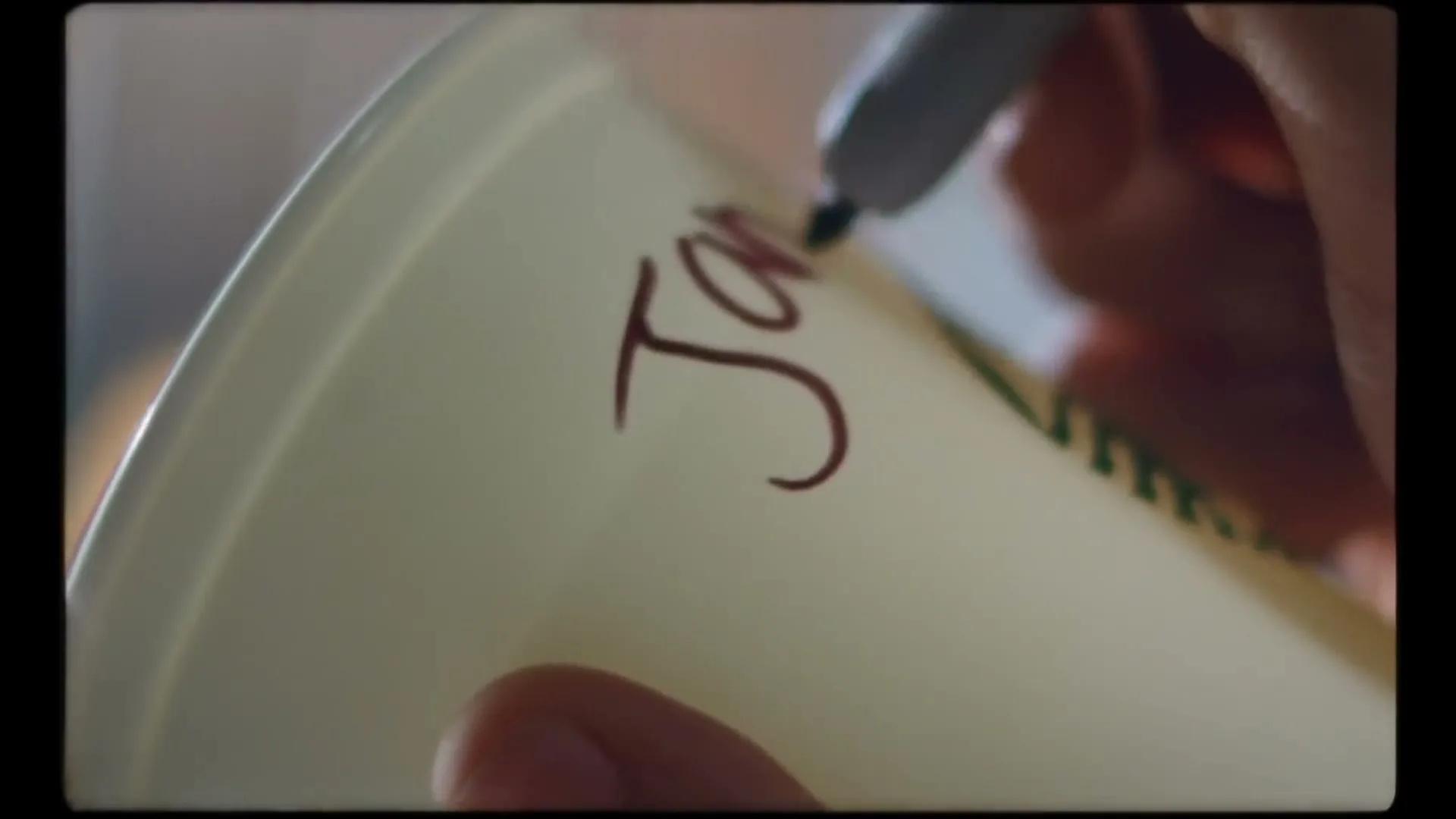 A barista's hand writes "Jan" on a Starbucks cup with a marker, in a close-up shot.