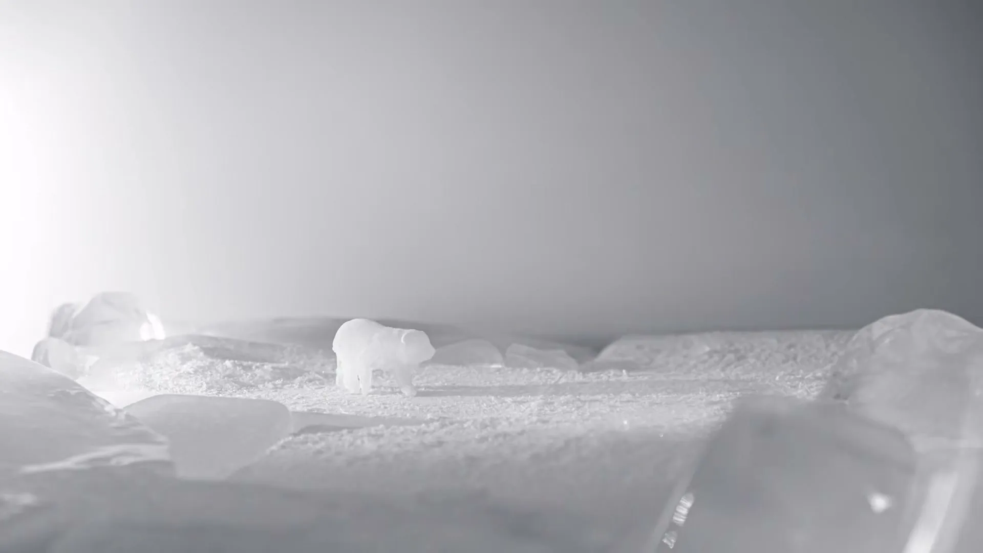 A small, translucent polar bear figurine walks across a landscape of ice and snow, slowly melting away.
