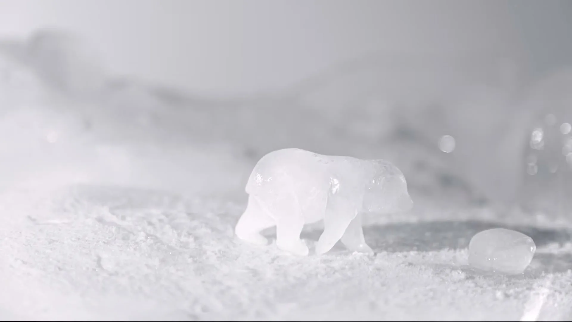 A small, translucent ice sculpture of a polar bear slowly melts on a white, textured surface, with water pooling around its base.