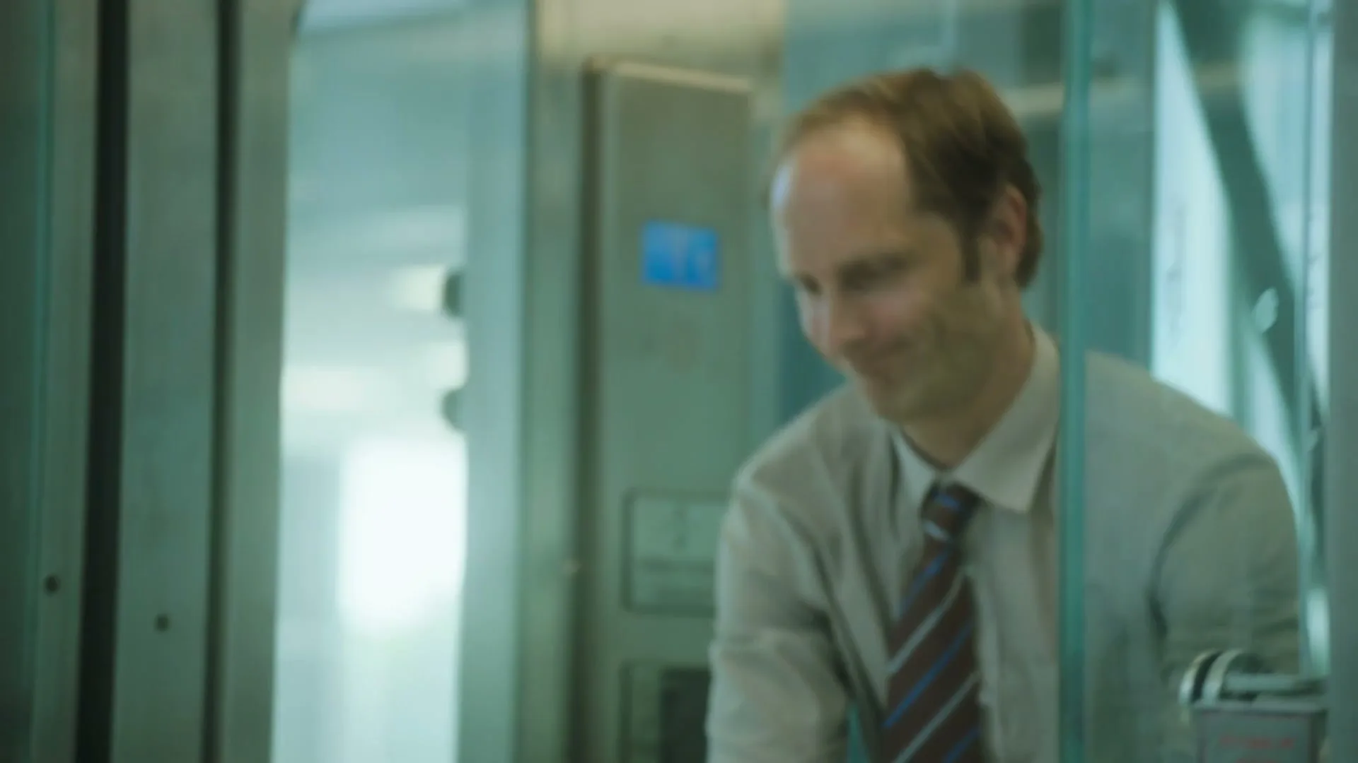 A red Yorkshire Tea teapot with an extra long spout is on a metal cart with cookies and sugar, as a man in a shirt and tie exits an elevator.