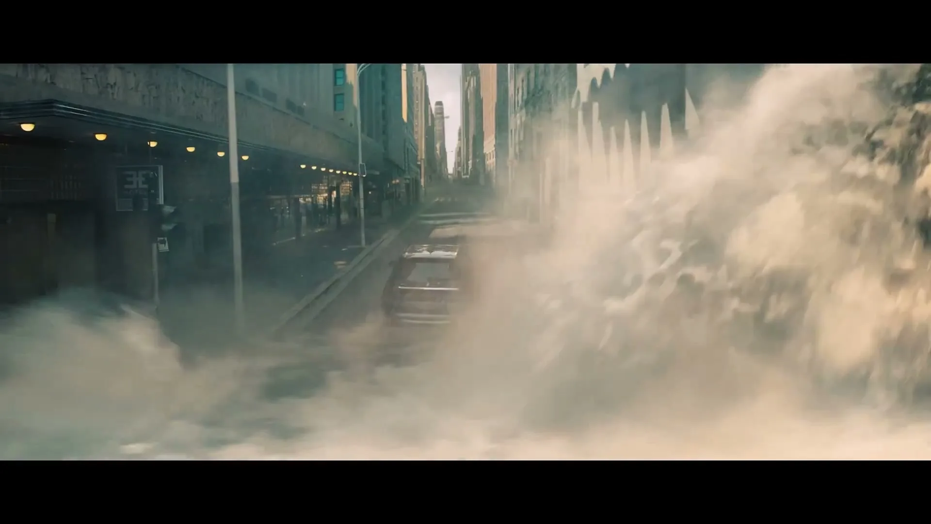 A black SUV drives down a city street as a massive wave of water crashes over the buildings on the right, creating a chaotic scene.