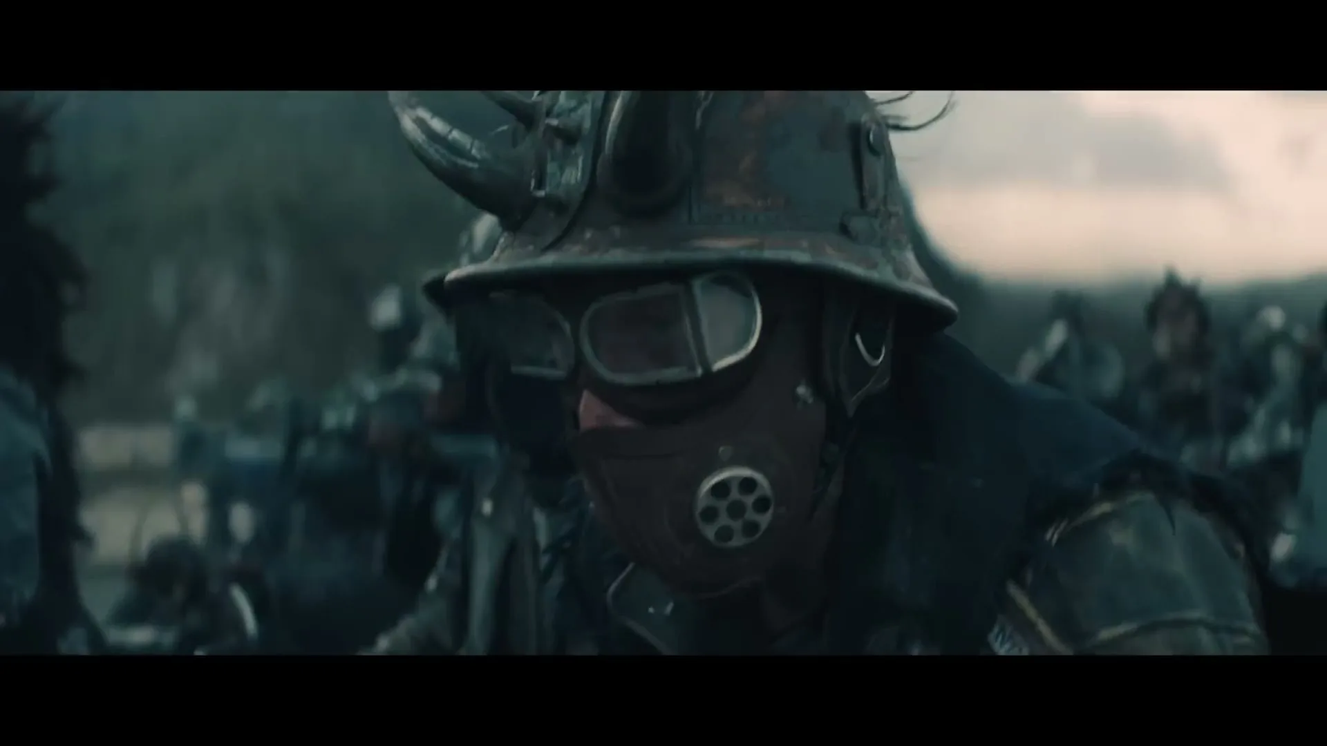 A person in a rusty helmet and gas mask looks down, surrounded by other similarly dressed figures in a desolate, war-torn landscape.