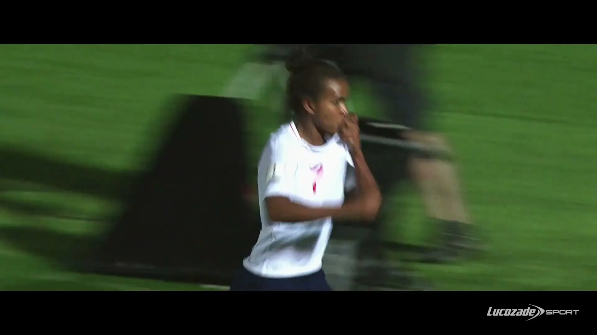 A female soccer player in a white jersey with number 7 runs across a green field, celebrating a goal during a night game.