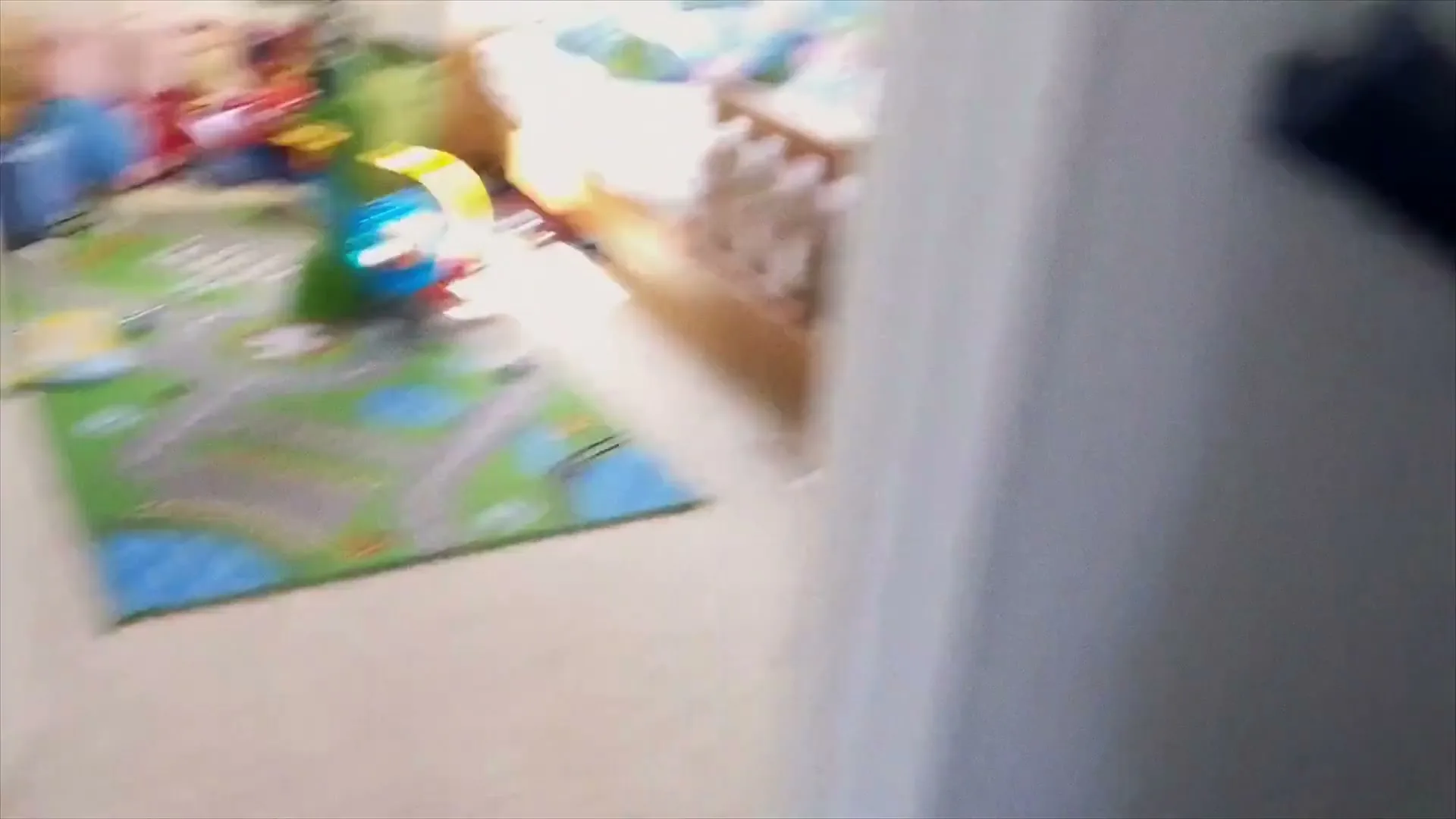 A blurry shot of a young boy in a white and black shirt, looking scared as he runs past the camera in a child's bedroom.