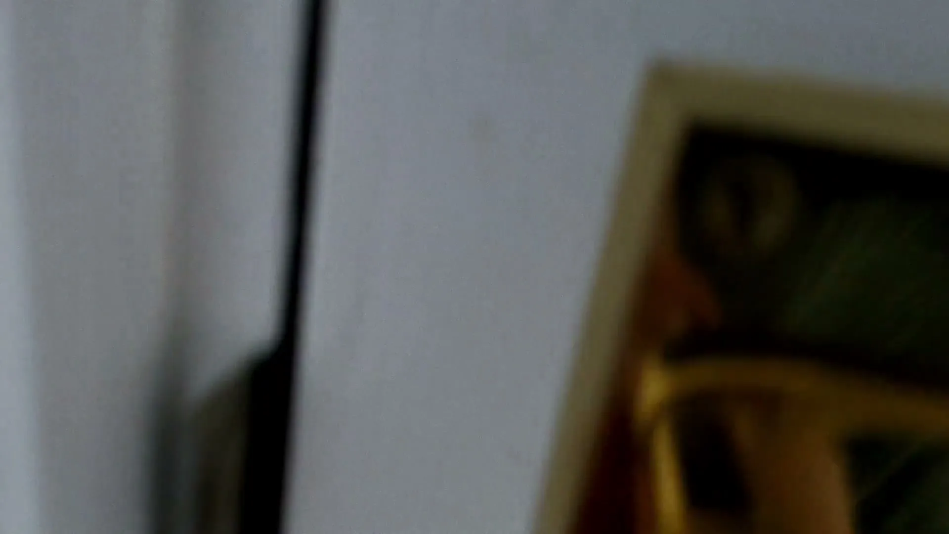 A blurry, extreme closeup shot shows a hand with a ring on its finger, closing a door with a golden handle, in an interior setting.