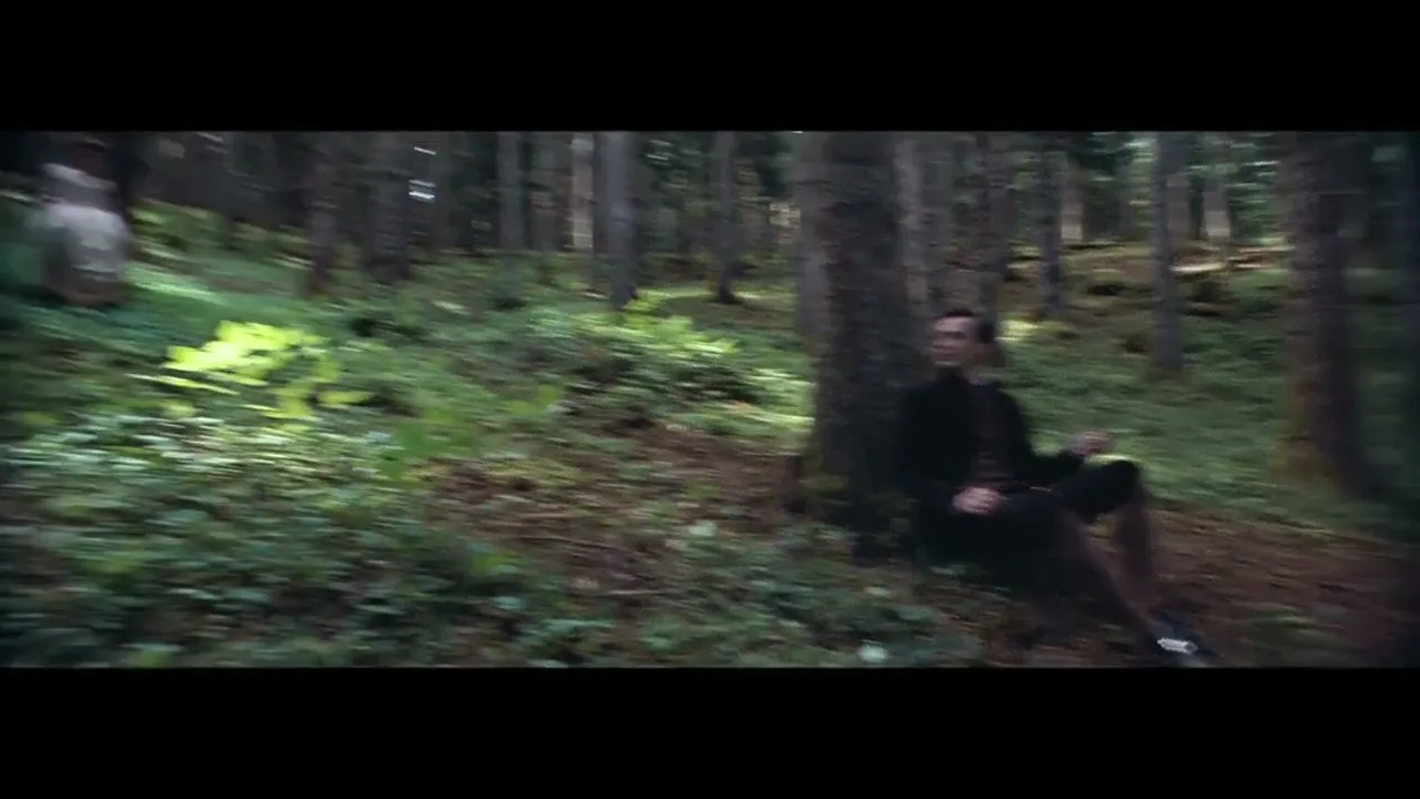 A man in period clothing sits against a tree in a forest, then a woman in a long dress walks through the sun-dappled woods.