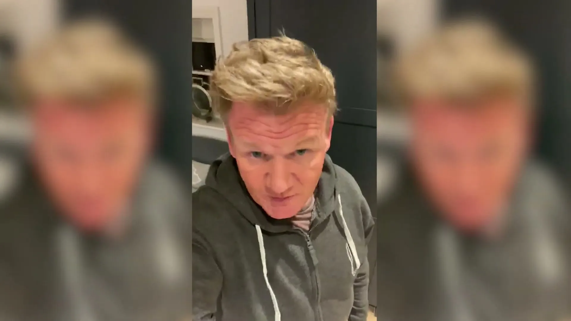 Gordon Ramsay, a male in his 50s, wearing a grey hoodie, speaks directly to the camera in a kitchen.