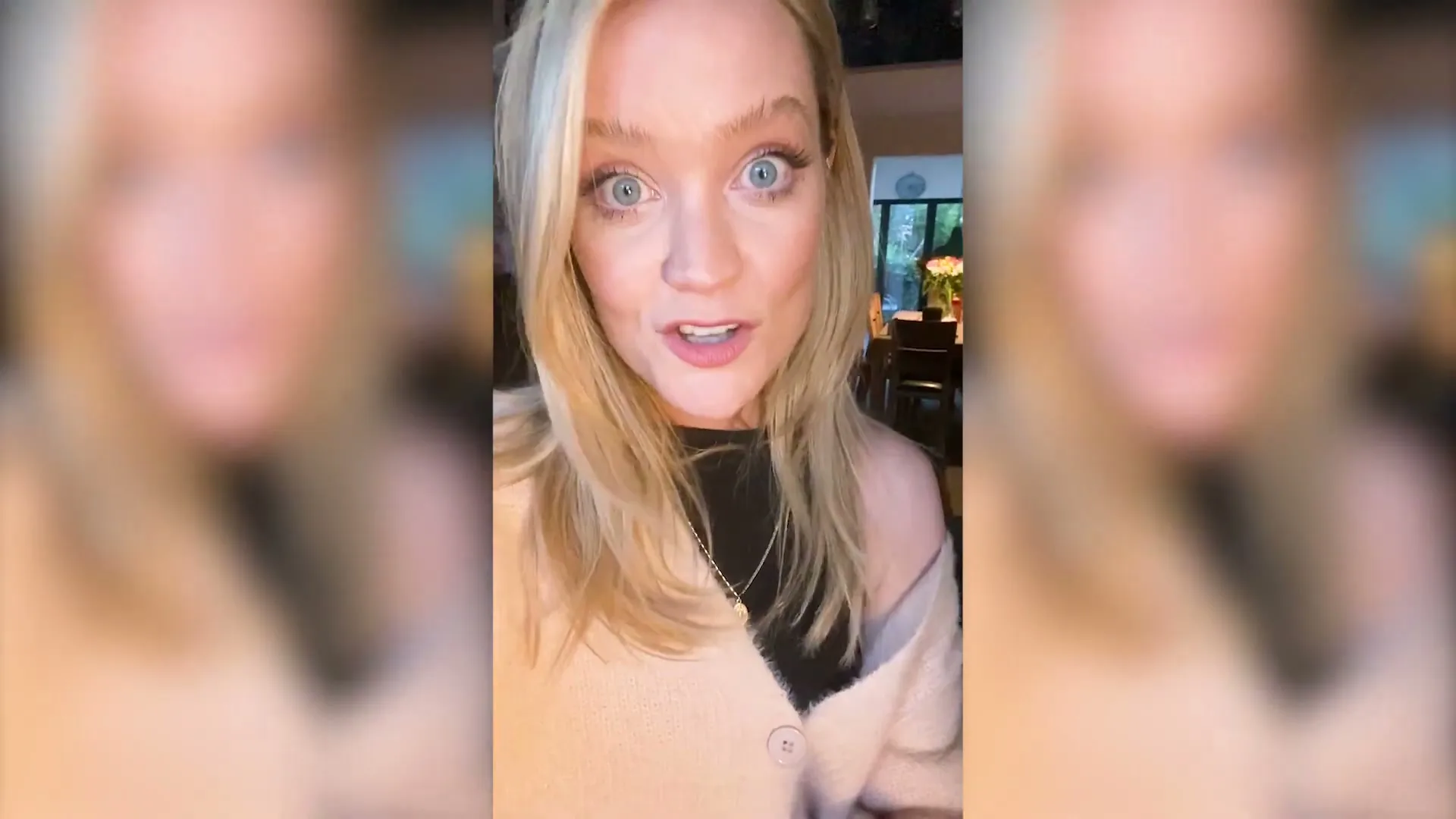 A blonde woman with blue eyes and a beige cardigan speaks directly to the camera in a medium shot, indoors.