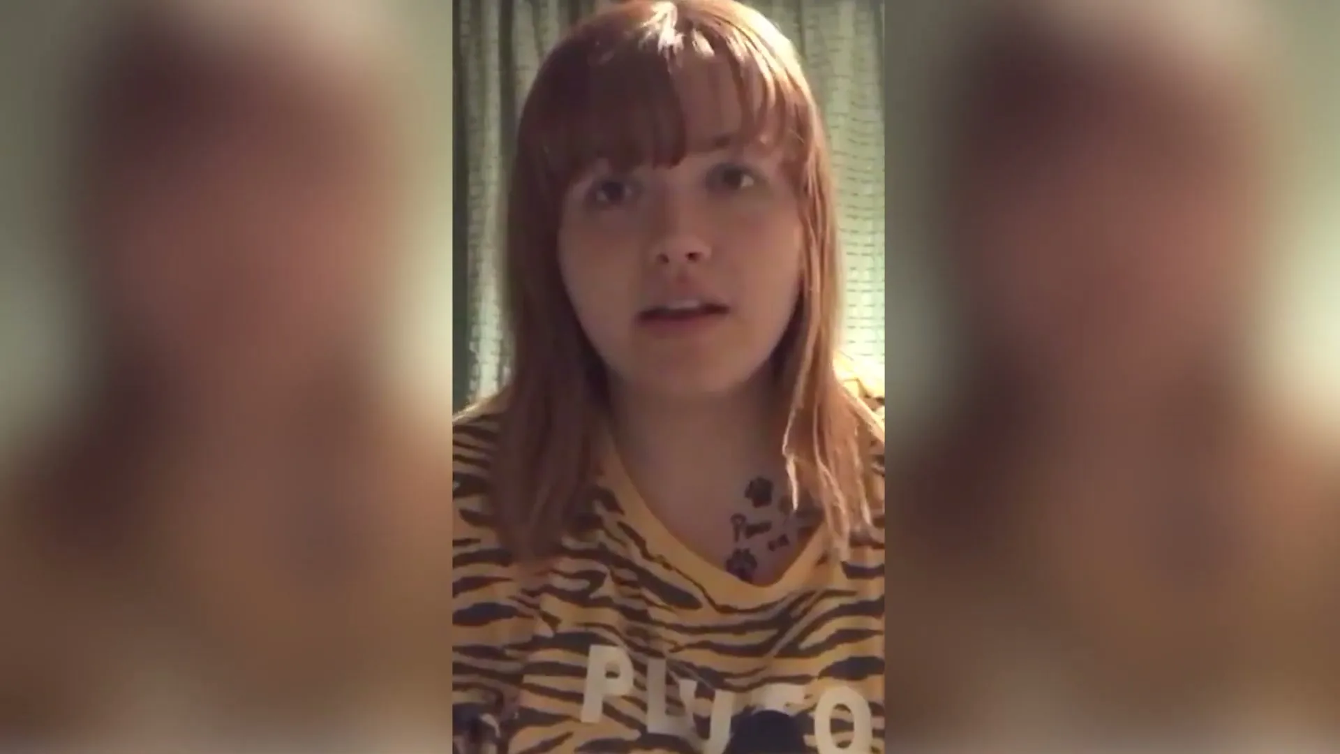 A young woman with red hair and a tiger-striped shirt looks directly at the camera, speaking in a close-up shot.